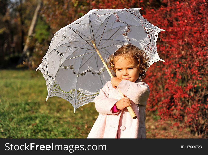 Little girl with umbrella in the park in autumn