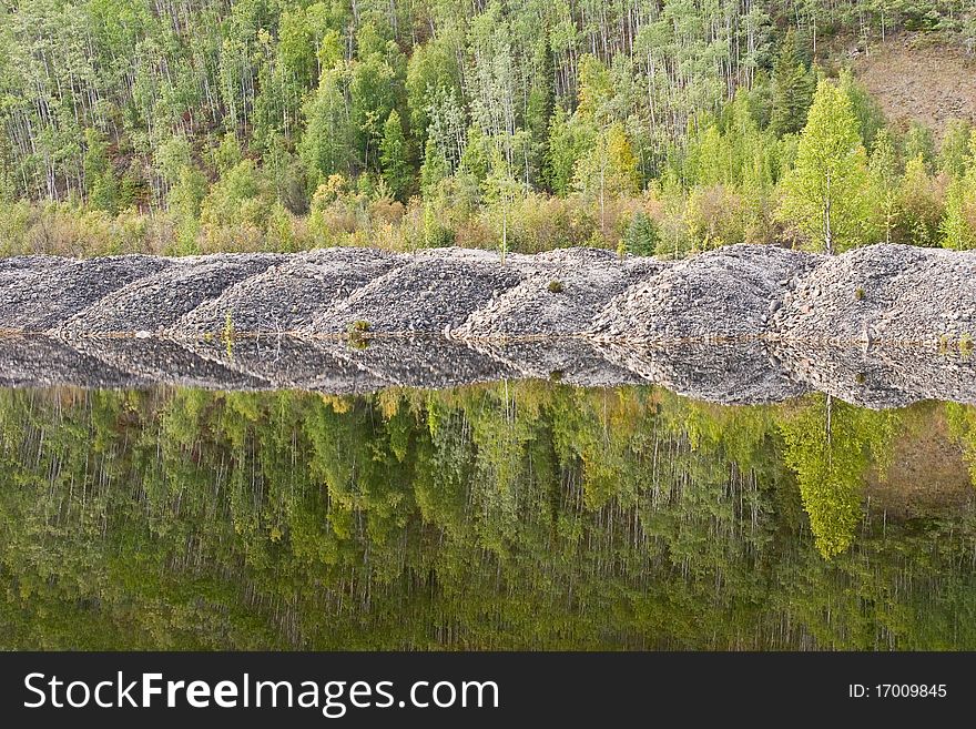 Mounds of gravel from a gold dredge are reflected in a tailings pond. Mounds of gravel from a gold dredge are reflected in a tailings pond