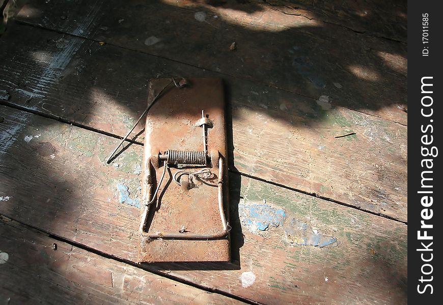 Rusty mousetrap on boards with scratches, at a sunlight in a shade