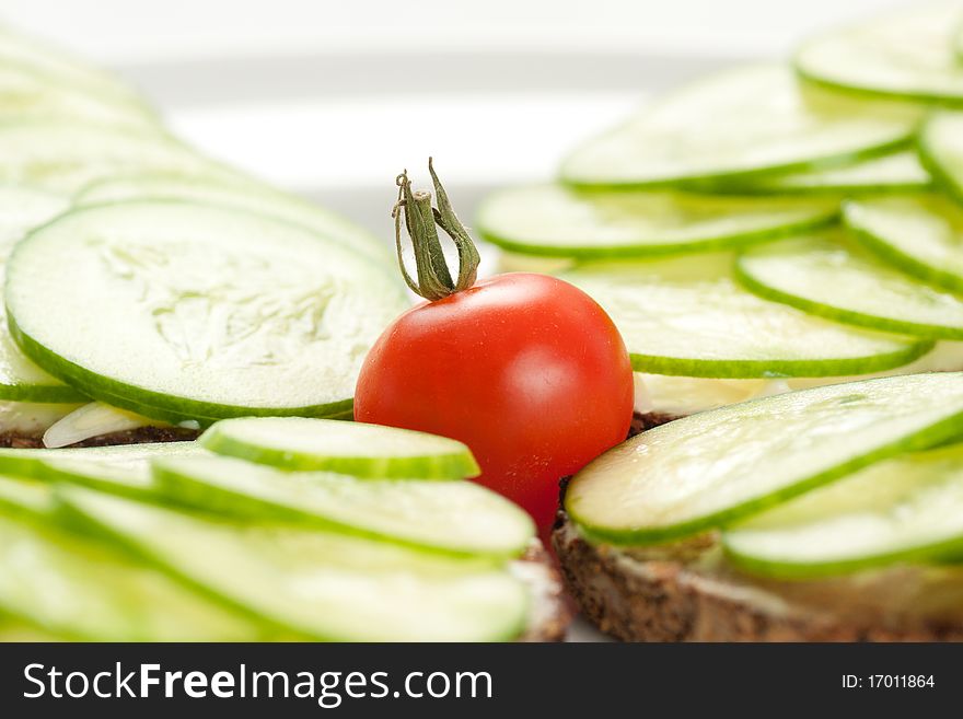 Small red tomato among pieces of rye bread with sliced cucumbers and cheese. Small red tomato among pieces of rye bread with sliced cucumbers and cheese