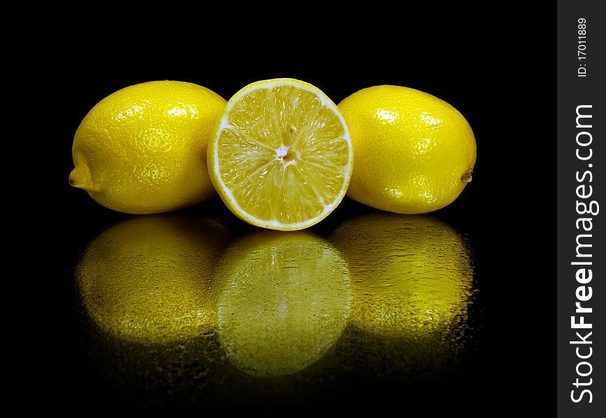 Fresh lemons on the black background with water drops