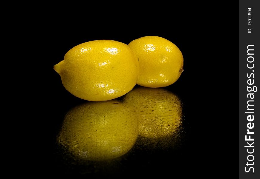 Fresh lemons on the black background with water drops
