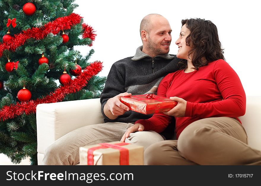 Young man giving a gift to his girlfriend near the Christmas tree. Young man giving a gift to his girlfriend near the Christmas tree