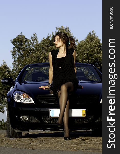 View of a beautiful woman next to sports car on a fashion pose. View of a beautiful woman next to sports car on a fashion pose.