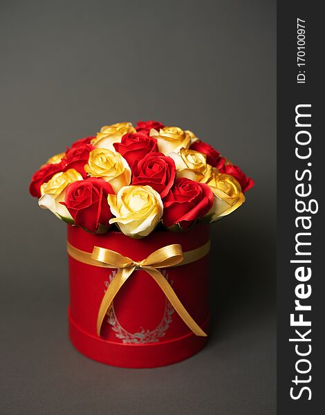 Flowers in bloom: A bouquet of red and golden roses in a red round box on a gray background.