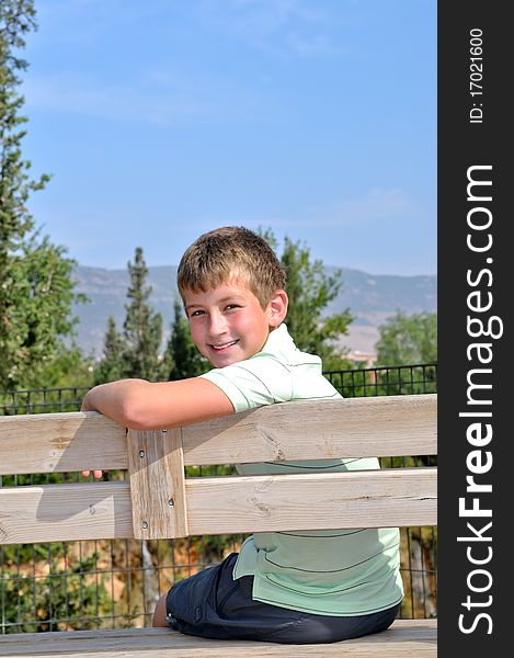 The boy is sitting on a park bench against the mountain landscape. The boy is sitting on a park bench against the mountain landscape