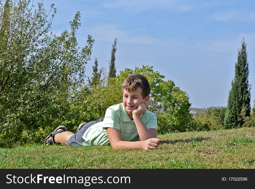 Portrait of a boy lying on the grass in the park and sustaining head on his hand. Portrait of a boy lying on the grass in the park and sustaining head on his hand