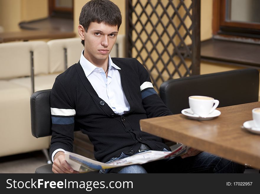 Young man with newspaper posing for camera across table with cup of coffee. Young man with newspaper posing for camera across table with cup of coffee