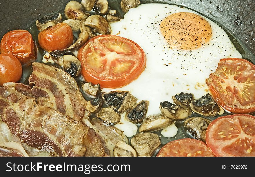 A macro image of a non-stick frying pan with egg, tomato, bacon and mushrooms. An image of a big breakfast. A macro image of a non-stick frying pan with egg, tomato, bacon and mushrooms. An image of a big breakfast.