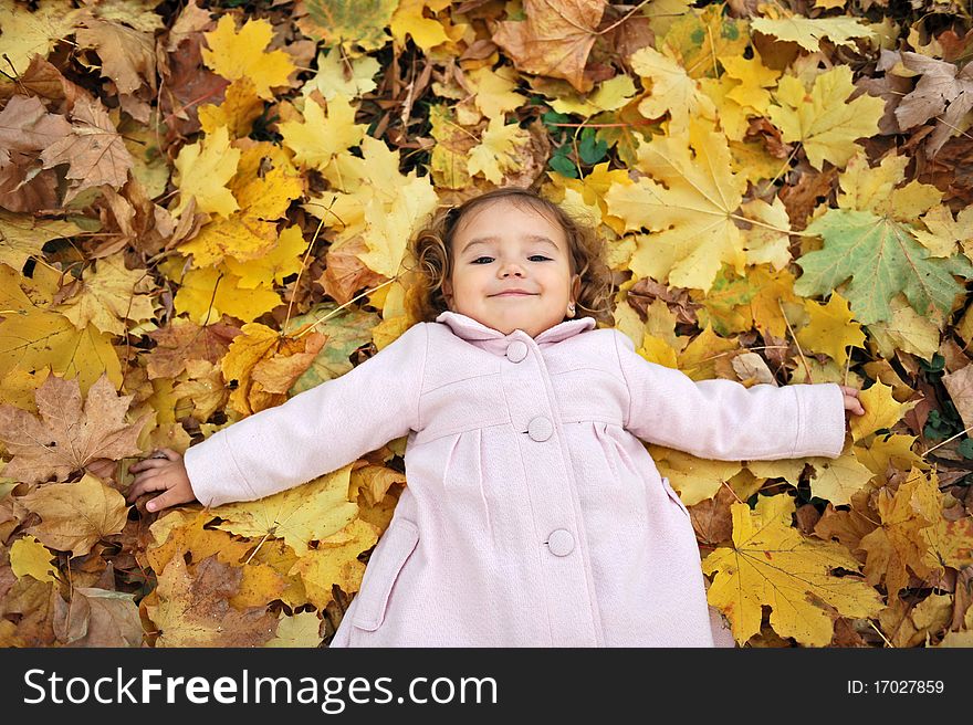 Little girl laying down on the leaves in the park in autumn. Little girl laying down on the leaves in the park in autumn