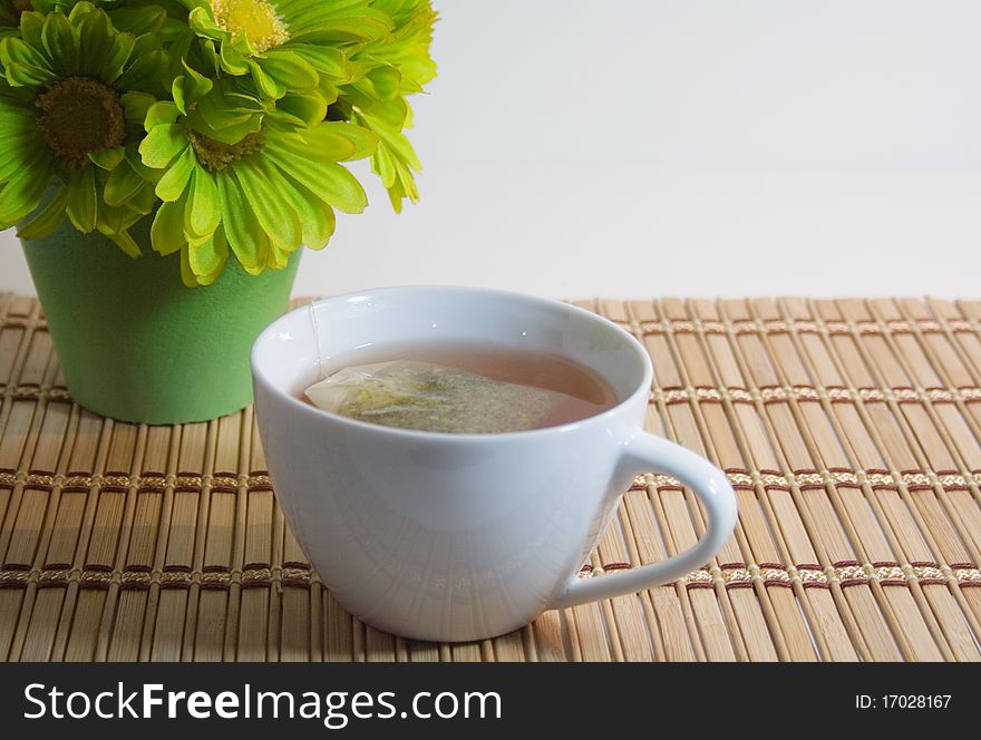 Cup of tea on bamboo with green flowers with white background