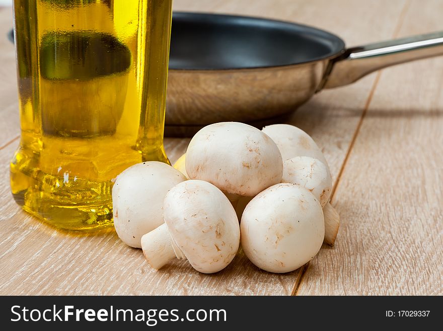 Button mushrooms, olive oil and frying pan on a wooden table. Button mushrooms, olive oil and frying pan on a wooden table