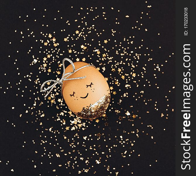 Creative Easter Egg With Cute Face And Sleepy Eyes On Black Background With Golden Glitter Confetti