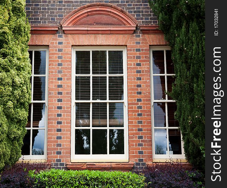 Windows in brick building framed by garden and fir trees. Windows in brick building framed by garden and fir trees.