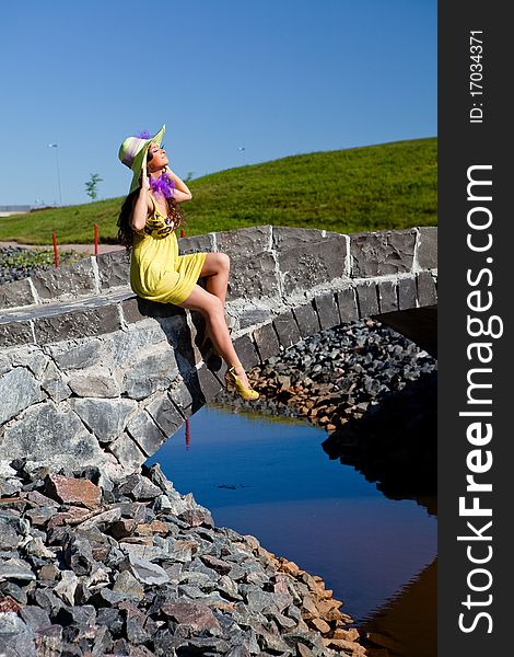 Happy Beautiful Girl Sitting On stone bridge in yellow dress