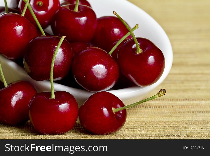 Red cherries in white spoon on yellow background