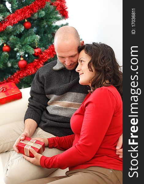 Young man giving a gift to his girlfriend near the Christmas tree. Young man giving a gift to his girlfriend near the Christmas tree