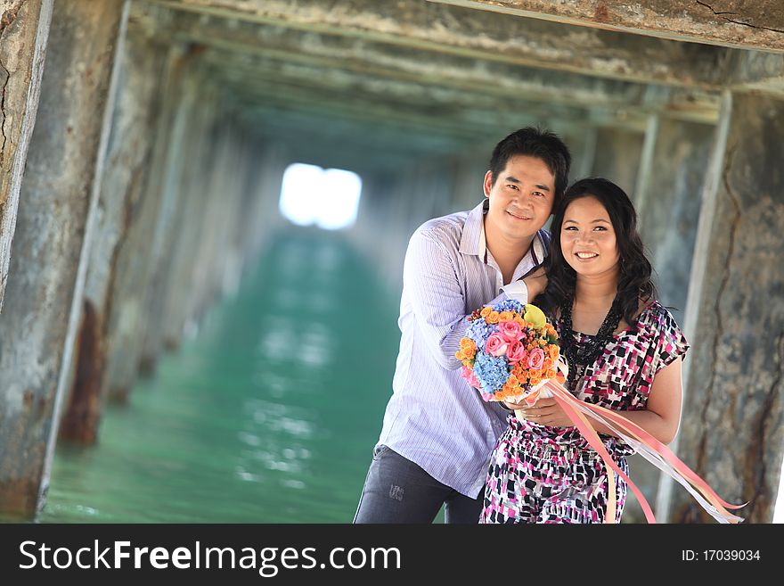 Couple standing outdoors smiling under pier on the beach. Couple standing outdoors smiling under pier on the beach