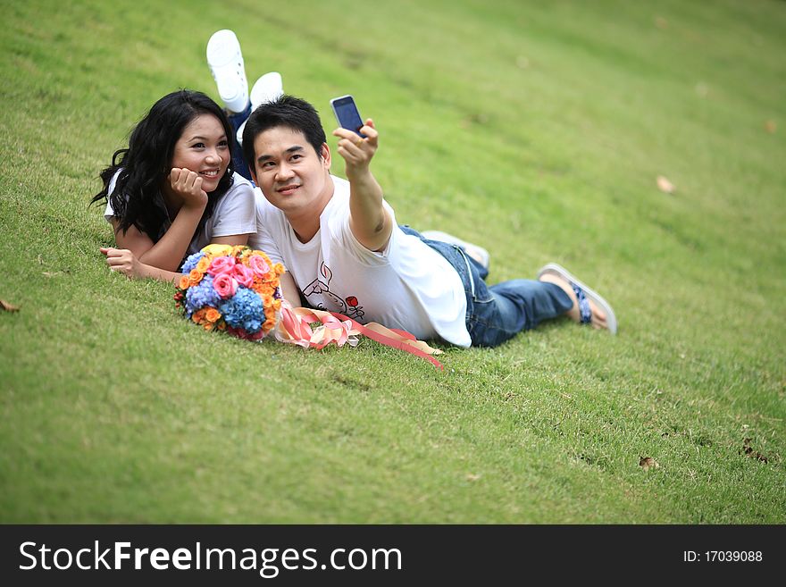 Ypung couples laying on grass and taking self portrait with mobile phone