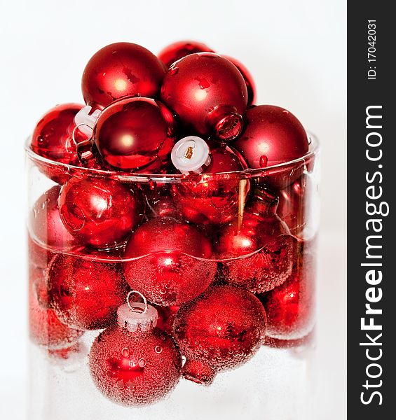 Clear glass cylinder holding a mound of red ball ornaments floating in water and covered with bubbles. Clear glass cylinder holding a mound of red ball ornaments floating in water and covered with bubbles