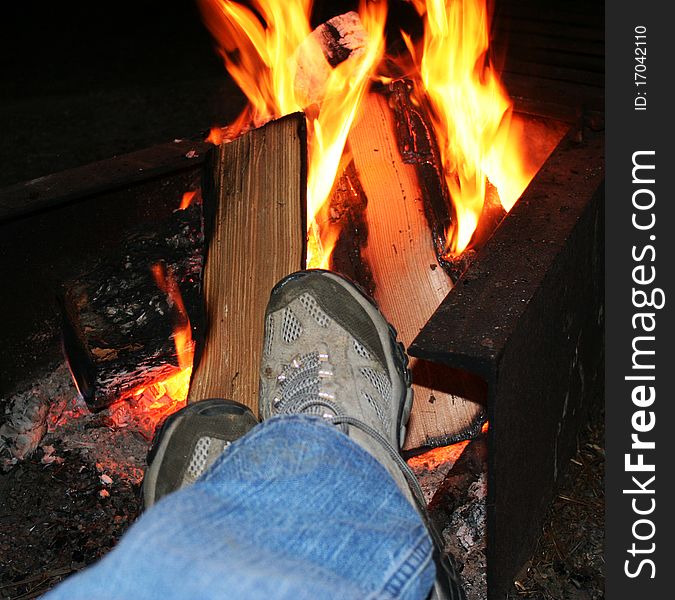 Legs and feet in hiking boots resting in front of a camp fire at night. Legs and feet in hiking boots resting in front of a camp fire at night