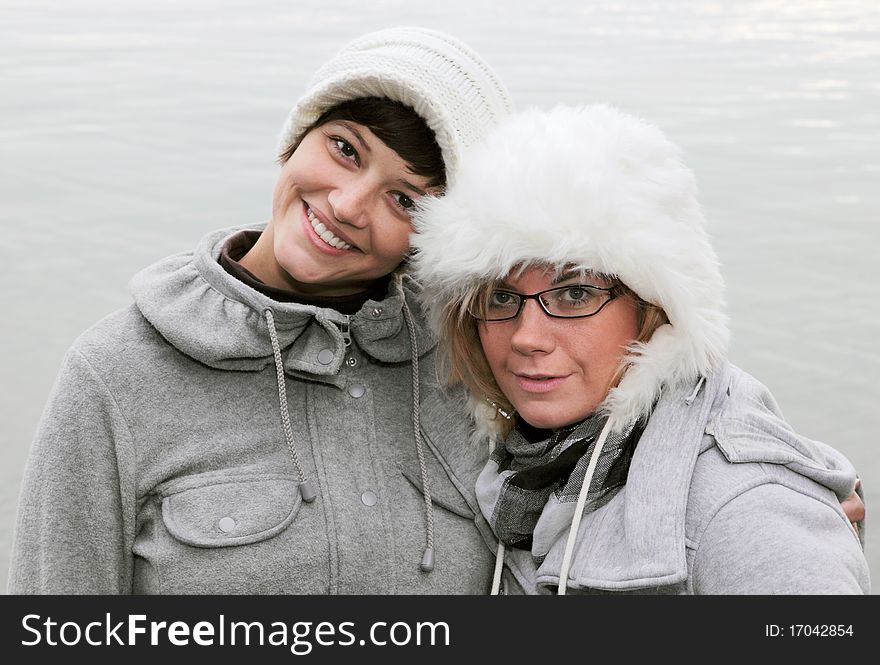 Winter outdoor shot at a lake of two young, pretty women with white caps, funny smiling into the camera. Winter outdoor shot at a lake of two young, pretty women with white caps, funny smiling into the camera.