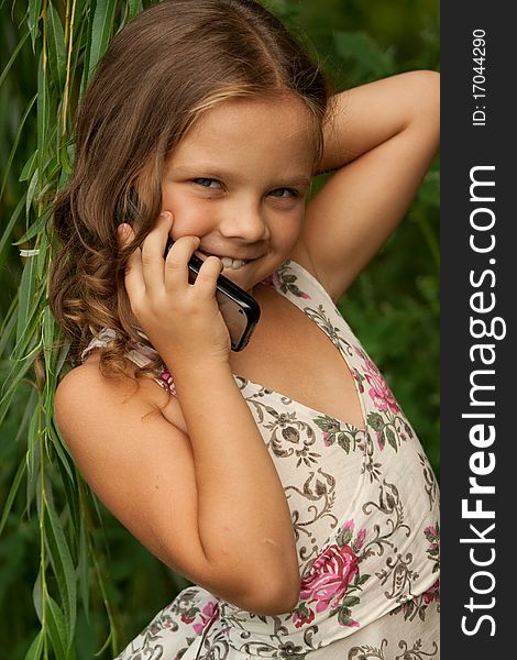 The small happy girl with a flowing hair, a mobile phone in a hand, in a nature background. The small happy girl with a flowing hair, a mobile phone in a hand, in a nature background.