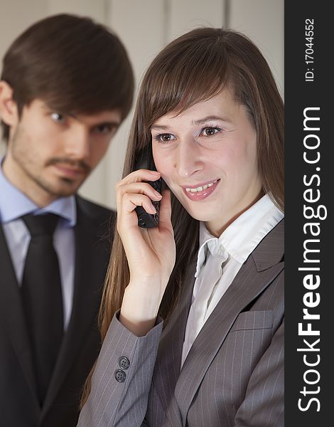 Businesswoman on phone in foreground - businessman to be ruled by jealousy. Focus on woman. Businesswoman on phone in foreground - businessman to be ruled by jealousy. Focus on woman