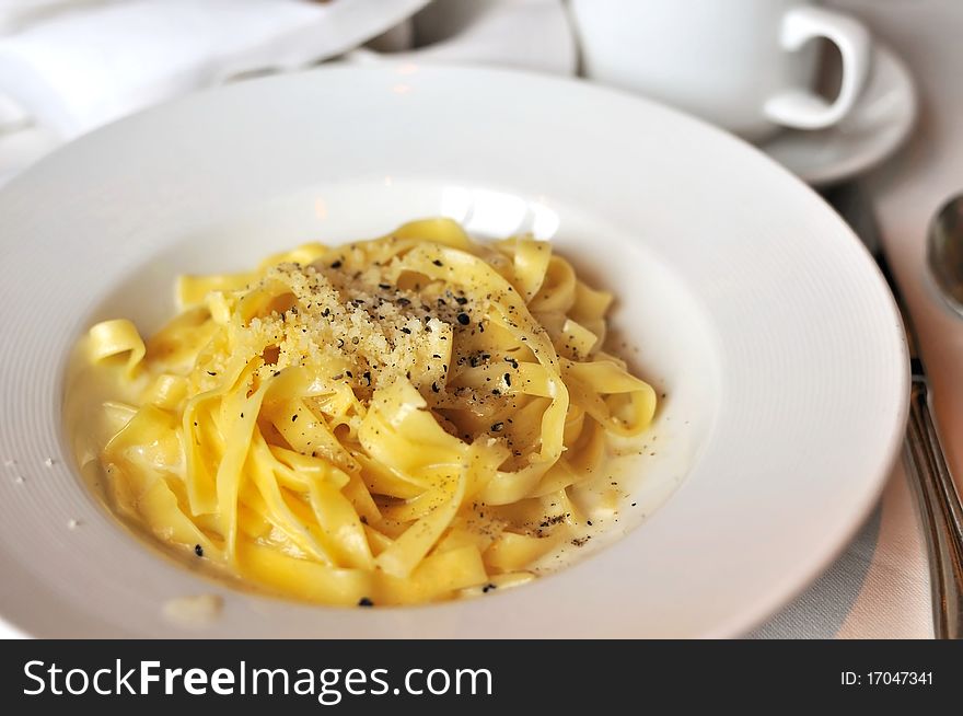 Delicious Italian style fettuccine topped with shredded cheese served on white plate.