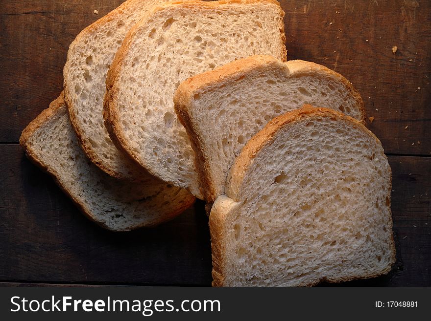 Few pieces of sliced white bread lying on dark wooden background. Few pieces of sliced white bread lying on dark wooden background