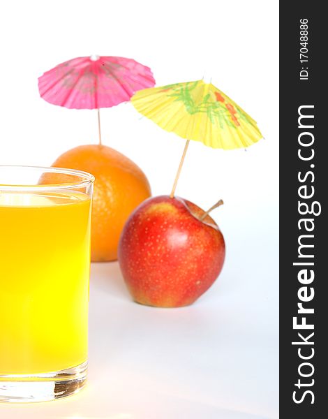 Orange and apple with small paper sunshades near glass of fruit juice on white background
