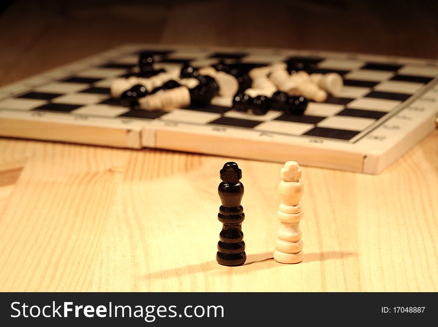 Chess concept. Two chessmen standing near chess board on wooden background. Chess concept. Two chessmen standing near chess board on wooden background
