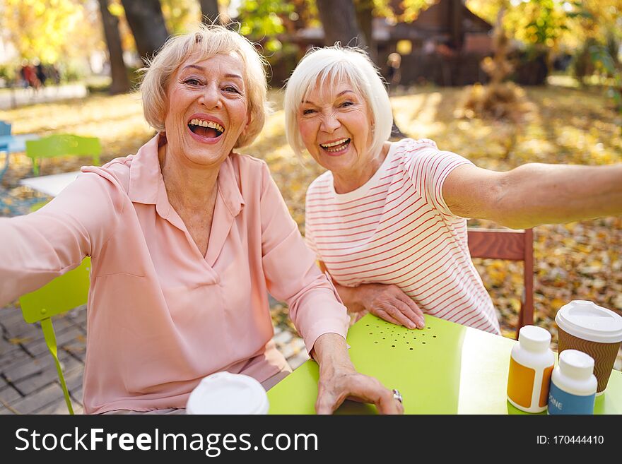 Beautiful old women laughing sitting in the park cafe together on the autumn day. Beautiful old women laughing sitting in the park cafe together on the autumn day