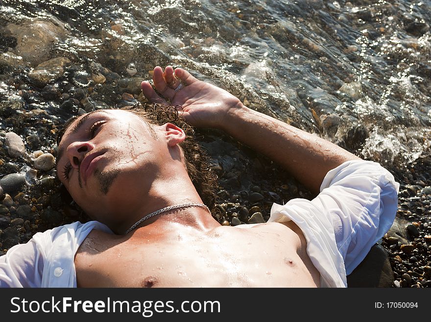 Young man lies on seacoast at water