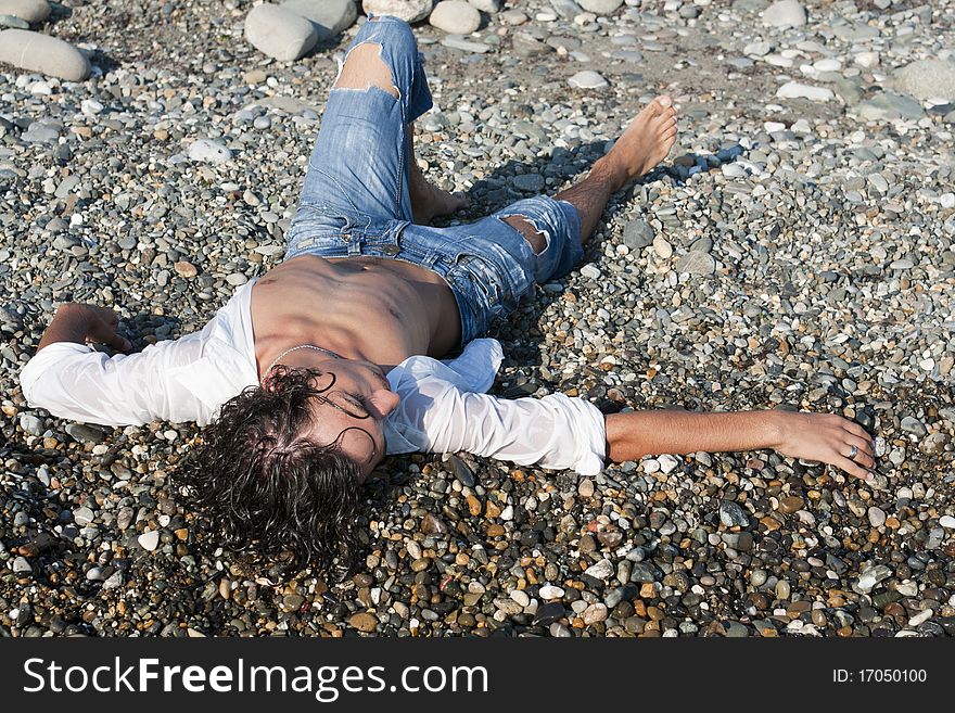 Young man lies on coastline on pebble