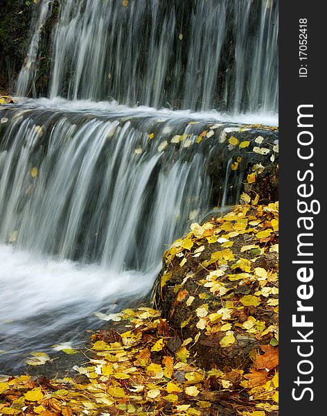 Waterfalls, a cascade of water flow, the stones are covered with fallen yellow leaves, autumn. Waterfalls, a cascade of water flow, the stones are covered with fallen yellow leaves, autumn