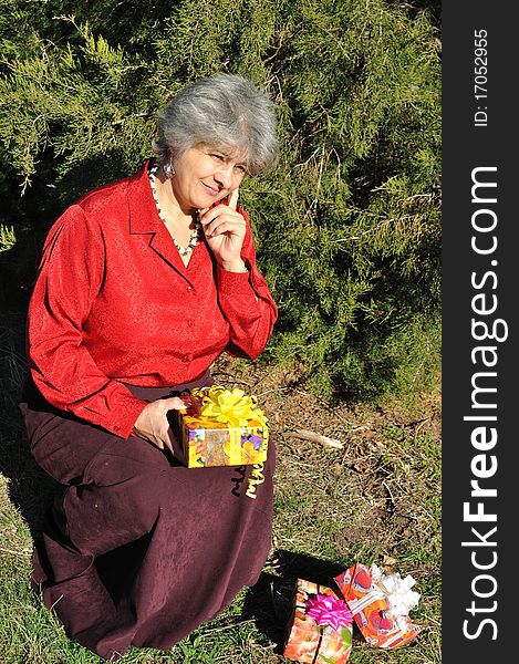 Puzzled, the old woman holds a lot of gifts, amid trees