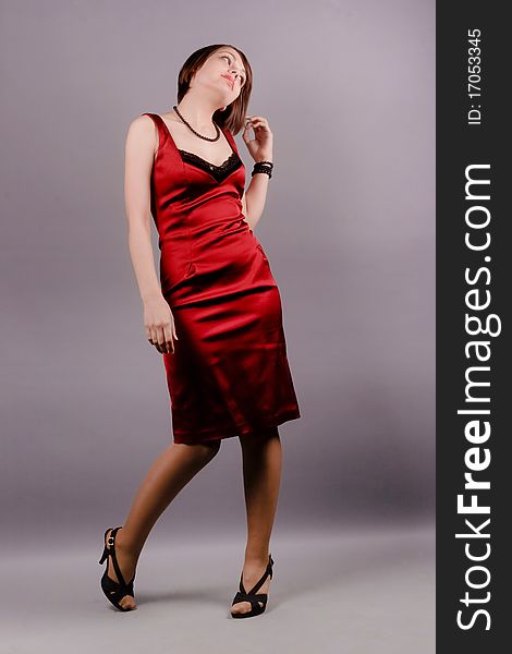 Portrait of a young beautiful pensive dreaming woman in red dress in full length. Studio shot on a gray background. Portrait of a young beautiful pensive dreaming woman in red dress in full length. Studio shot on a gray background.