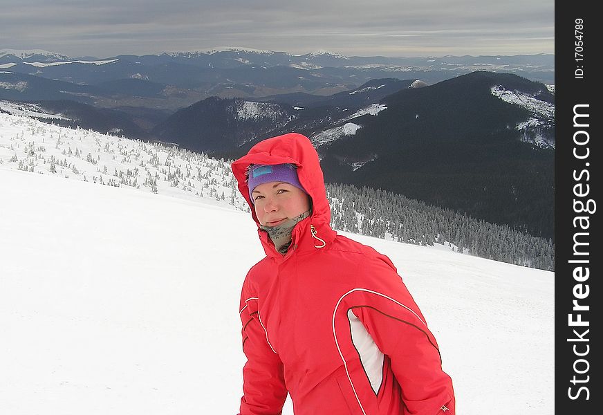 Portrait of young woman in a red ski-wear on the background of mountains. Portrait of young woman in a red ski-wear on the background of mountains