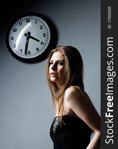 Attractive young woman and clock on gray background