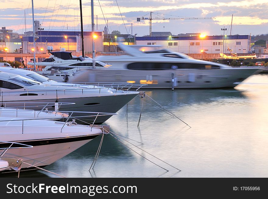 A motor yacht is sailing away from a marina dock at dusk. A motor yacht is sailing away from a marina dock at dusk