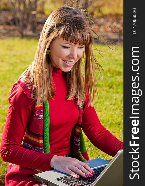 Smiling beautiful girl with a laptop on the grass in autumn park