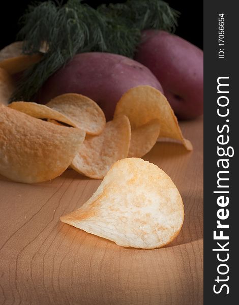 Potato chips with a potato on a kitchen board.