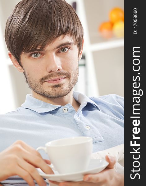 Young man holding cup tea while sitting on sofa at home. Young man holding cup tea while sitting on sofa at home