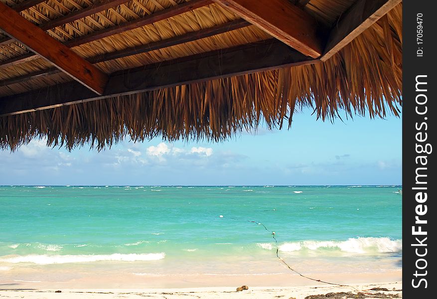 View from under palm leaves shelter onto tropical beach of a Caribbean island