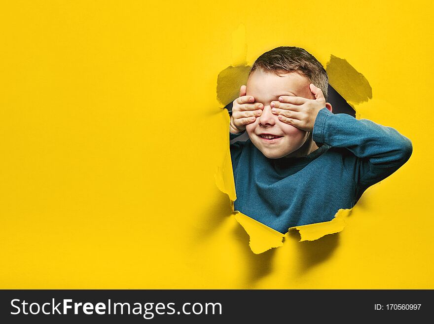Happy cute boy is having fun played on black background wall. climbs through a hole in the paper. Bright photo of a boy.