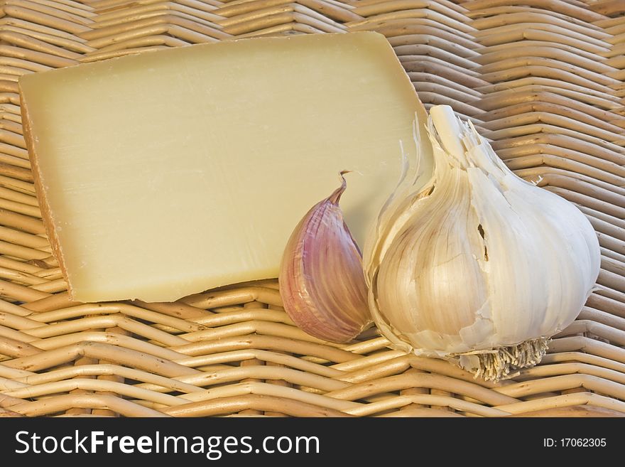 A close up of hard cheese,a clove and bulb of garlic on a wicker background. A close up of hard cheese,a clove and bulb of garlic on a wicker background
