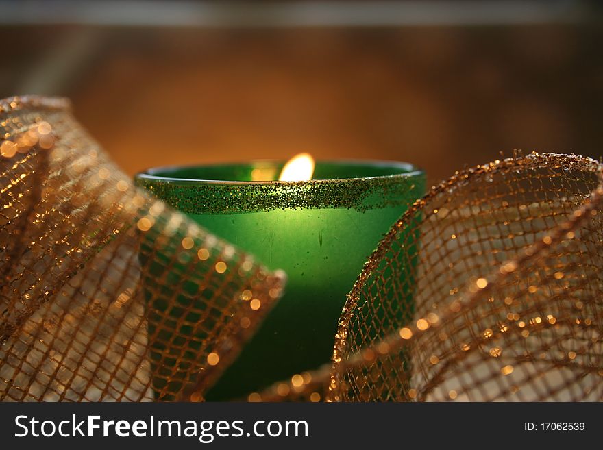 Closeup of a candle burning in a green glass votive holder surrounded by gold mesh ribbon. Closeup of a candle burning in a green glass votive holder surrounded by gold mesh ribbon.