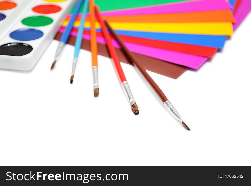 Brushes, paints and a color paper for creativity over white