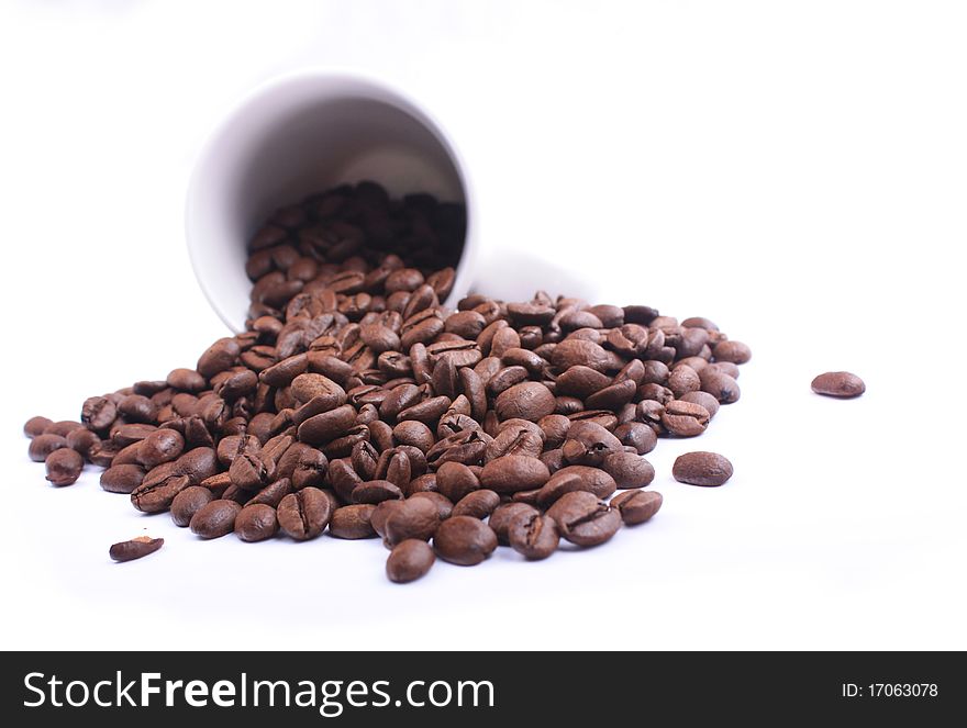 A coffee cup full of coffee beans knocked over on a white background. A coffee cup full of coffee beans knocked over on a white background